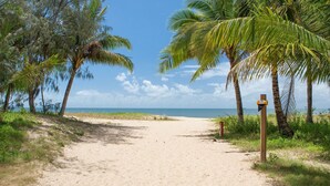 Un sentier de plage sablonneux bordé de palmiers, offrant une vue dégagée sur l’océan.