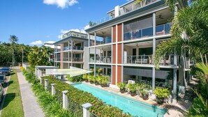 Un hôtel à plusieurs étages doté d’une piscine, d’un espace extérieur aménagé et d’une végétation luxuriante.