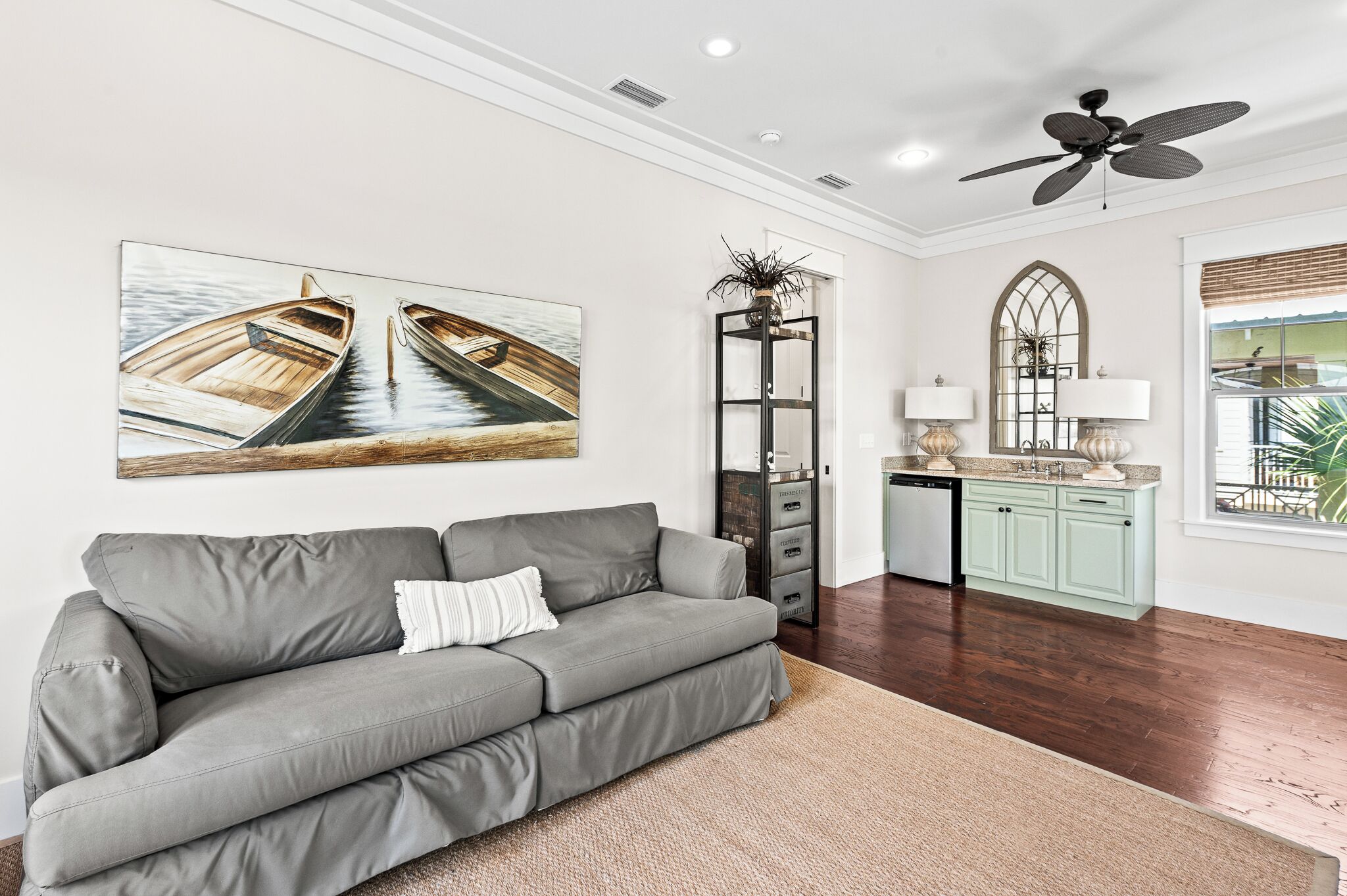 A modern living room with a grey sofa, a ceiling fan, and a large window with a view.