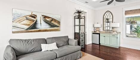 A modern living room with a grey sofa, a ceiling fan, and a large window with a view.