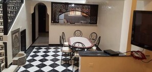 A dining area with a checkered floor, a table with four chairs, a decorative partition, and a television on a stand.