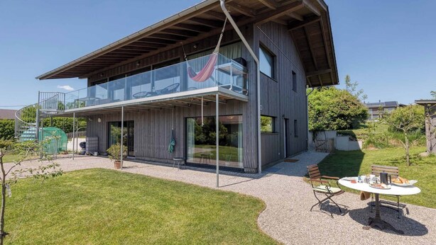 Een modern huis met twee verdiepingen, een ruim balkon, een hangmat en een eethoek met tuinmeubilair.
