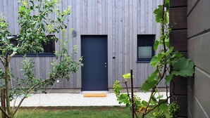 Een modern gebouw met een donkerblauwe deur, een klein raam en een grindpad dat naar de ingang leidt.