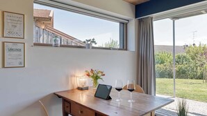 Een kamer met een houten bureau, een tablet, twee wijnglazen en een vaas met bloemen. Er hangen certificaten aan de muur en er is uitzicht op het buitenleven.
