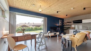 Een moderne woonruimte met een houten plafond, een eethoek met tafel en stoelen, een bank, een televisie en een keuken.