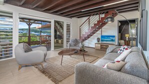A spacious living area with a modern staircase, a sofa, a coffee table, and a view of the outdoors. - Bwa Canon (Le Diamant)