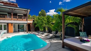 A pool area with a wooden deck, lounge chairs, and a covered seating area. - Bwa Canon (Le Diamant)