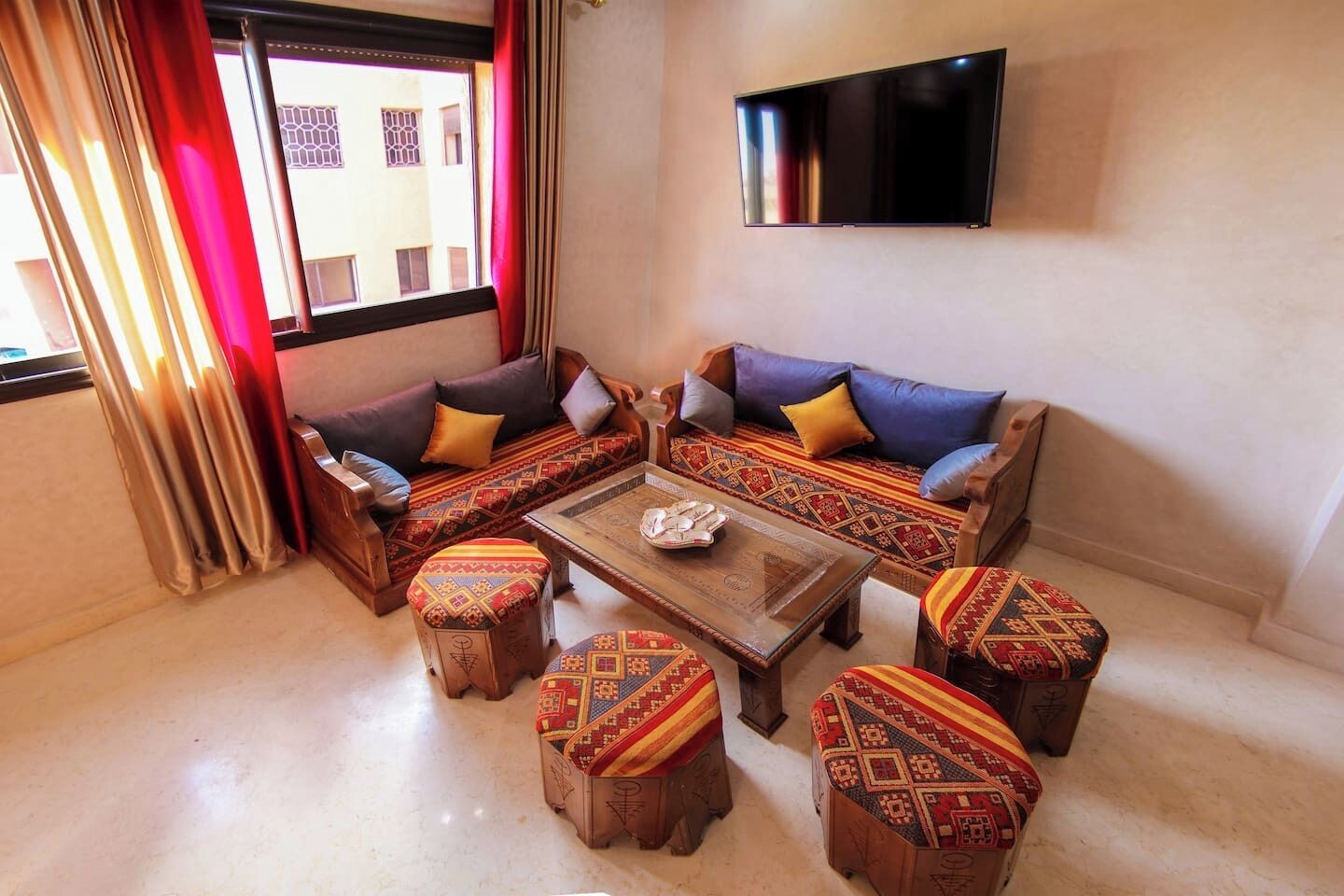A living room with a sofa set, ottomans, a coffee table, and a flat-screen TV mounted on the wall.
