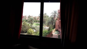 A view from a window with curtains, overlooking a courtyard with palm trees and a building with balconies. - Quiet stay - MARRAKECH : Apartment 87 m² SWIMMING POOL, FREE WIFI, PARKING (Marrakech)