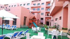 A courtyard with lounge chairs, a children's play area, and a building with multiple balconies. - Quiet stay - MARRAKECH : Apartment 87 m² SWIMMING POOL, FREE WIFI, PARKING (Marrakech)
