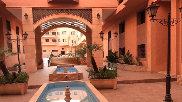 A courtyard with a central pool, surrounded by potted plants and a staircase leading to a building. - Quiet stay - MARRAKECH : Apartment 87 m² SWIMMING POOL, FREE WIFI, PARKING (Marrakech)