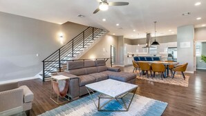 Ein geräumiges Wohnzimmer mit einer modernen Couch, einem Essbereich mit gelben Stühlen und einer Treppe, die zu einer oberen Etage führt.