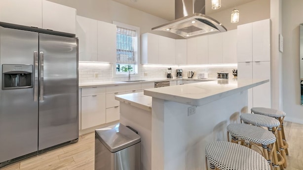 A modern kitchen with stainless steel appliances, a central island with bar stools, and pendant lighting. - 3-Level Brand New Townhouse in Mid City (New Orleans)