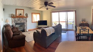 A living room with a fireplace, a television, a sofa, a dining table with chairs, and a sliding glass door leading to an outdoor patio.