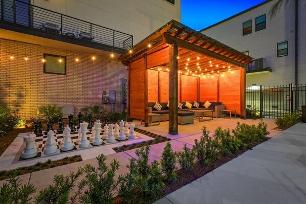 A covered outdoor seating area with a chessboard and lounge furniture.