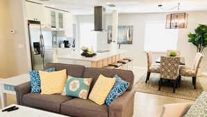 A modern living room with a brown sofa, a white coffee table, and a dining area with patterned chairs. - Charming Bungalow, remodeled, heated pool, walk to the beach (Naples)