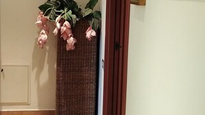 Een gang met een decoratieve plant, een houten deur en een schilderij aan de muur.