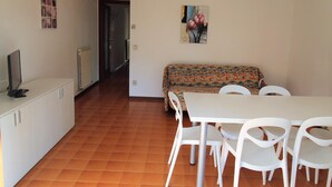 A dining area with a white table and chairs, a patterned sofa, and a painting on the wall. - villa MARISA 2 - Lignano (Lignano Sabbiadoro)