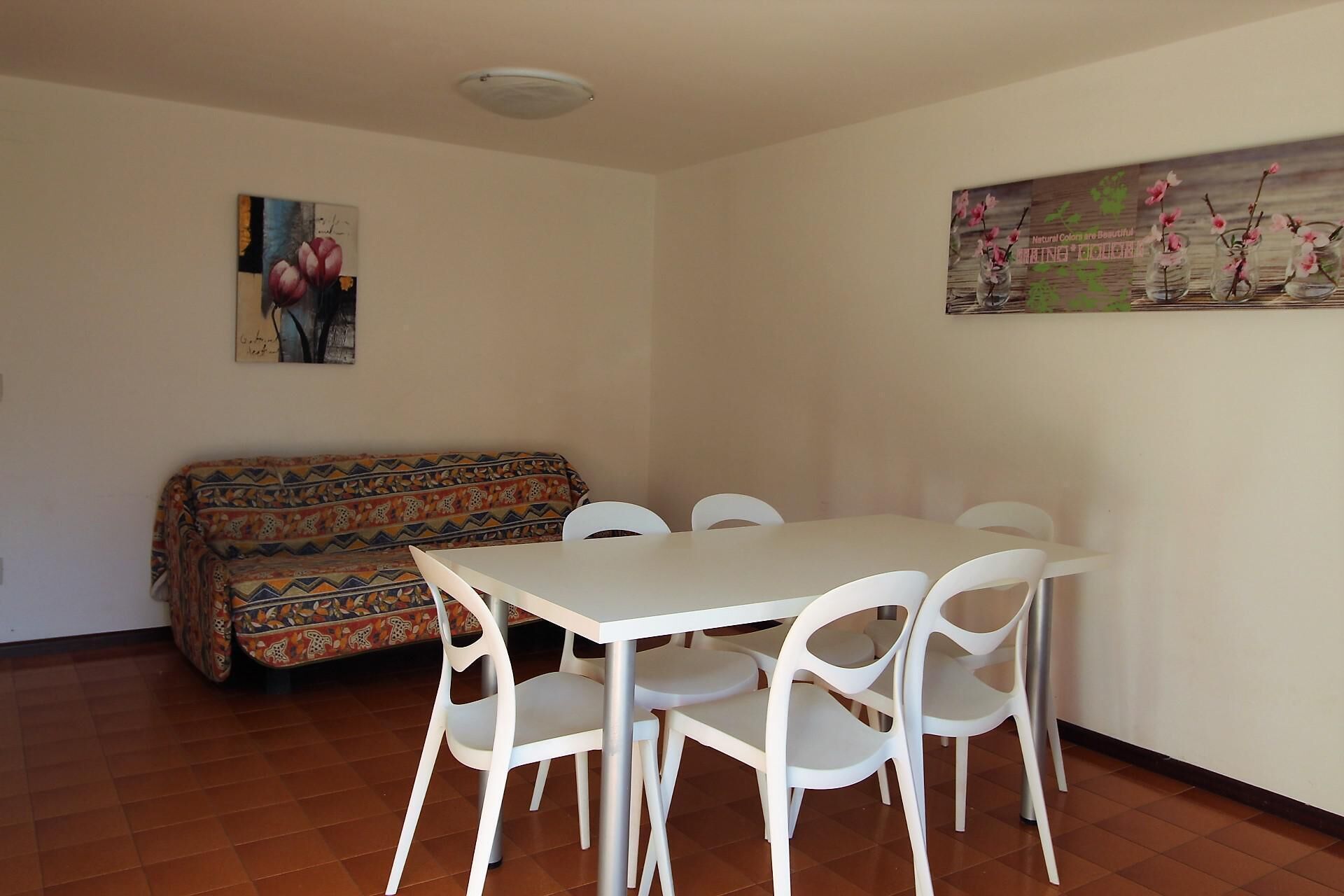 Ein Essbereich mit Tisch und Stühlen, einer gemusterten Couch und zwei Wandbildern.