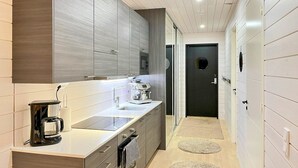 Una cocina moderna con una encimera larga, electrodomésticos integrados y una puerta oscura al fondo del pasillo.