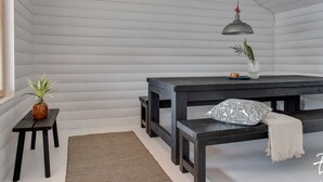 Una habitación con techo de listones de madera, una mesa de madera oscura con bancos, una lámpara colgante y una pequeña planta en maceta.