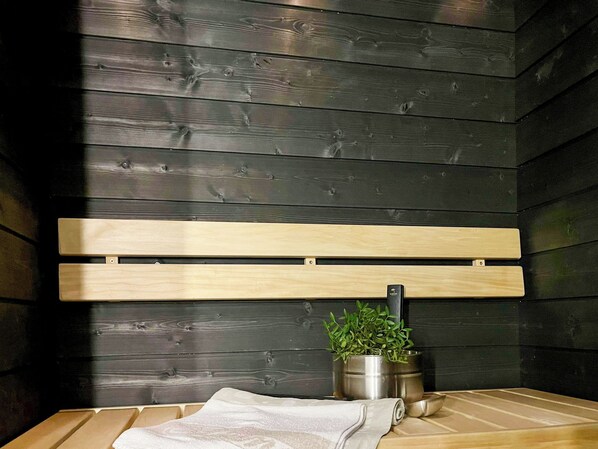 Un banc en bois, un pot en métal et une serviette enroulée, le tout posé sur un plancher en bois.