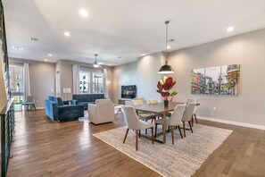 Un salon moderne avec un coin repas, comprenant une grande table, des canapés et un téléviseur.