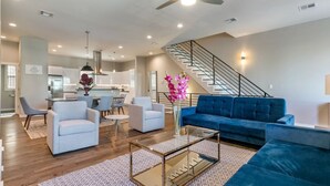 A spacious living area with a blue sofa, two armchairs, a coffee table, and a staircase leading to an upper level.