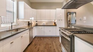 A modern kitchen with white cabinets, a stainless steel range, and a wooden floor.