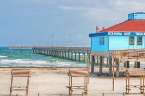 Un muelle que se adentra en el océano, con un edificio a la derecha identificado con la leyenda "POCE-RENTAL BAIT TACKLE".