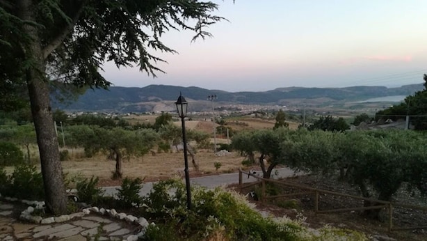A stone pathway leading to a rustic outdoor seating area with a lamp post, surrounded by greenery and overlooking a valley.
