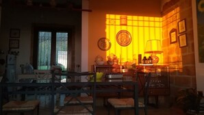 A dining area with a table and chairs, a window with bars, and a wall with framed pictures and a lamp.