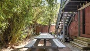 A picnic table in a backyard with a wooden fence and a red building in the background.