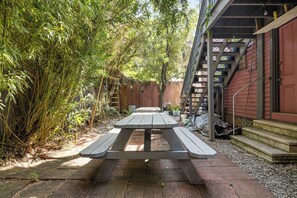 Una mesa de picnic en un patio trasero con una valla de madera y un edificio rojo al fondo.