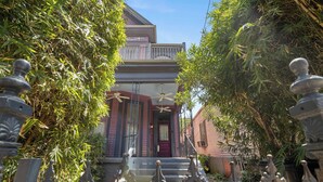 A house with a red door, a balcony, and a garden with decorative metal sculptures.