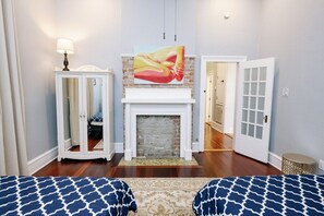 A room with a fireplace, a mirror cabinet, a bed with patterned bedding, and a painting on the wall. - Claiborne Victorian Mansion, by Historic Getaways (New Orleans)