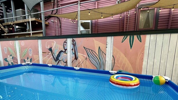 An indoor swimming pool with a tiled floor, surrounded by a wooden deck and a mural on the wall.