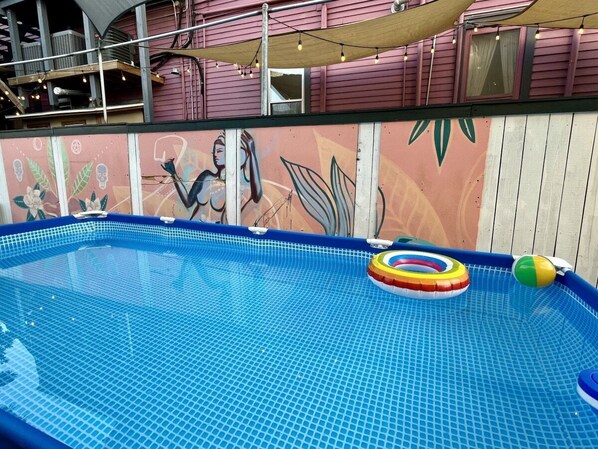 Una piscina interior con suelo de baldosas, rodeada por una terraza de madera y un mural en la pared.