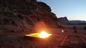 Un paysage désertique avec un feu qui brûle sur le sol, un tapis et une falaise rocheuse en arrière-plan.