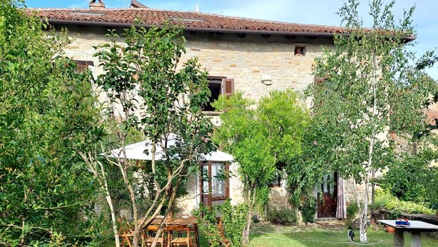 A stone building with a tiled roof, surrounded by a well-maintained garden with wooden furniture and a small table. - Casa Clelia: the gem in the heart of the Langhe (Loazzolo)