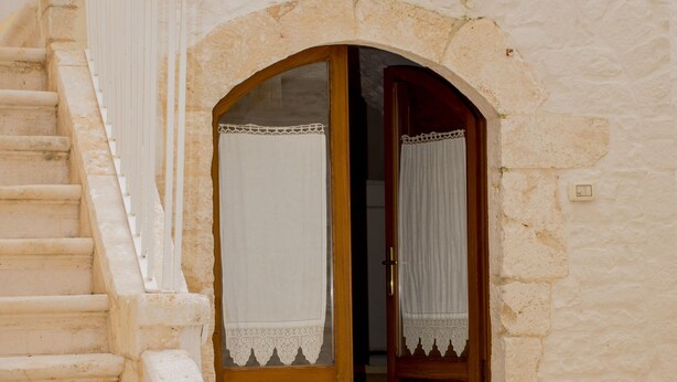 A stone building with a wooden staircase and a door with white curtains.