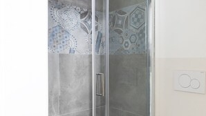 A shower with a glass door, patterned tiles, and a wall-mounted light switch. - Cute Studio in Old Town (Como)