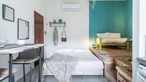 A compact bedroom with a bed, a small table, and a bench. There is a shelf with a plant and a hanging coat. - Cute Studio in Old Town (Como)