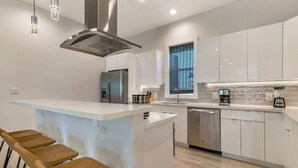Une cuisine moderne dotée d’un îlot central, d’appareils électroménagers en acier inoxydable et de luminaires suspendus.