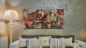 A living room with a beige sofa, striped pillows, a heart-shaped throw pillow, a white floor lamp, and a floral painting on the wall. - STELLA DELLE GRIGNE (Pasturo)