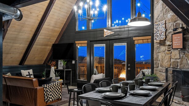 A cozy dining area with a wooden table set for four, a leather couch, and a stone wall with a fireplace.