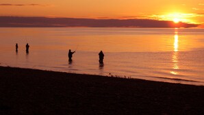 Atardecer sobre un cuerpo de agua tranquilo con cuatro personas pescando.