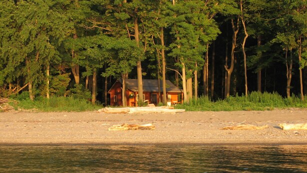 Una cabaña junto a un lago rodeada de árboles.