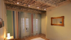Quarto com cama, mesa de cabeceira, espelho e janela com cortinas.