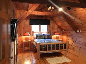 Ett mysigt sovrum i en stuga med träpanel, inrett med en säng, två sänglampor, ett fönster och en dörr.